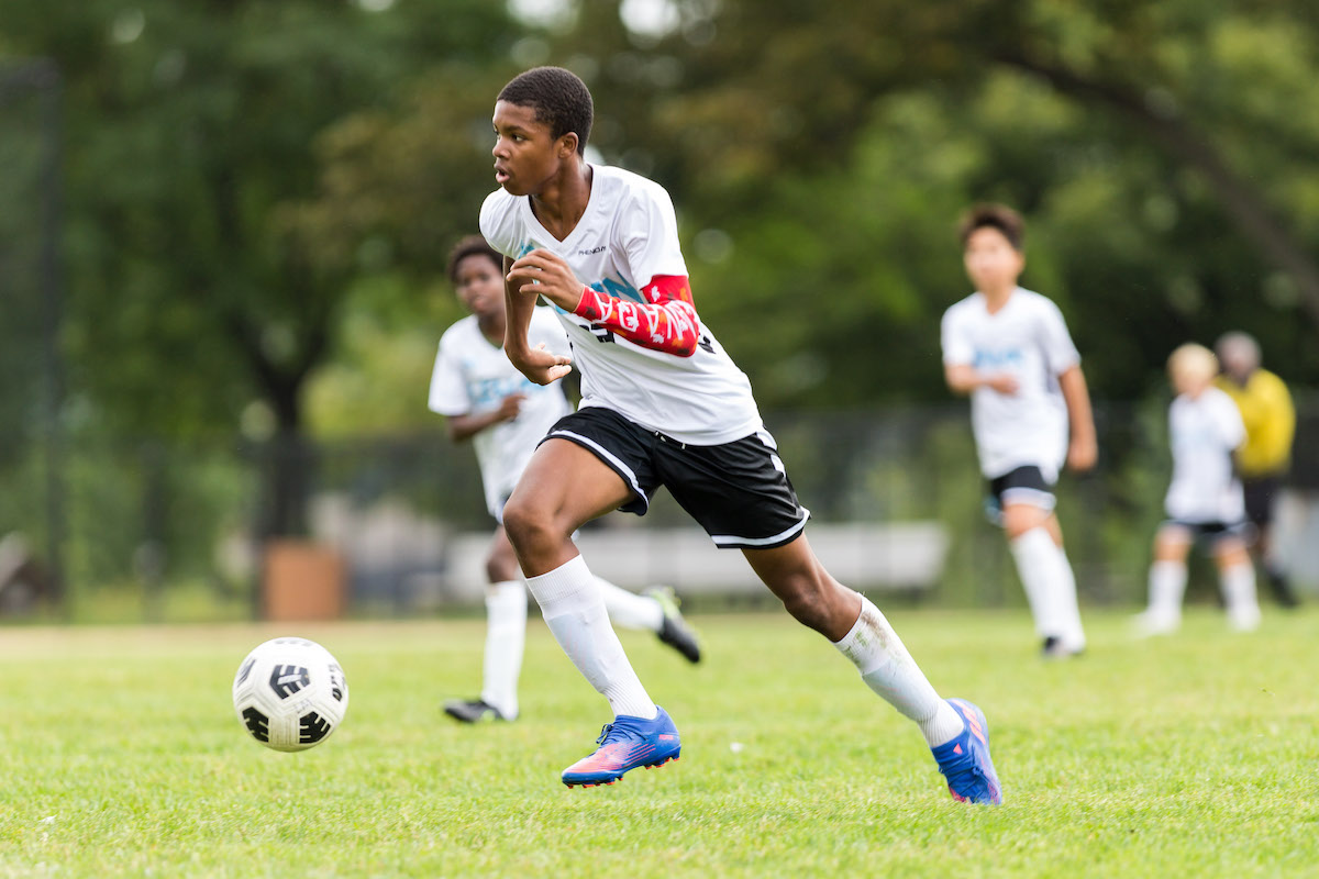 A student on the Middle 宝博体育 soccer team runs, kicking a ball in front of him. He is in a white and blue uniform.